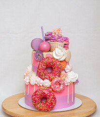 Pink ombre birthday cake with donuts, meringues and chocolate on neutral background. Cupcake on the top