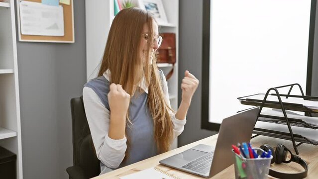 Yes! young blonde business woman, a true office winner, arms raised, celebrating her joyful and triumphant win. happy, excited and successful &ndash; the sweet smell of success!