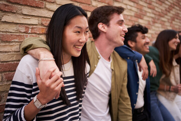 A group of young people are sitting in front of a brick wall, sharing smiles and happy gestures. They wear fun hats and travel sleeves, enjoying a fun event together