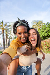 Vertical photo of Two happy women are standing next to a tree in the park, smiling as they take a selfie together. Their arms are stretched out, with the sky and plants in the background