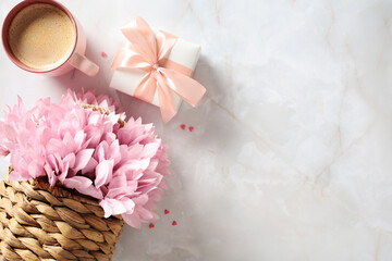 Rattan basket with pink flowers, gift box and cup of coffee, and heart-shaped confetti on stone table. Happy Mother's Day greeting card design. International Women's Day, feminine birthday concept.