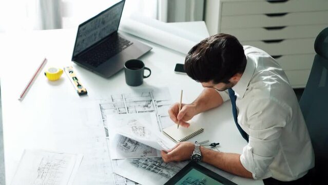 Architect engineer using laptop planning house design at office while sitting at meeting table with blueprint and equipment scatter around.Skilled civil engineer working at blueprint. Alimentation.