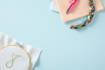 Flat lay composition with cross stitch embroidery and sewing material on blue background
