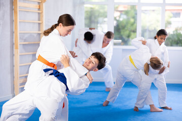 Concentrated teen girl in kimono honing grappling techniques during kumite with boy at group karate...