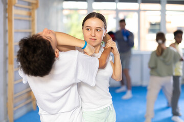 Boy and girl training self-defense techniques in group in studio..
