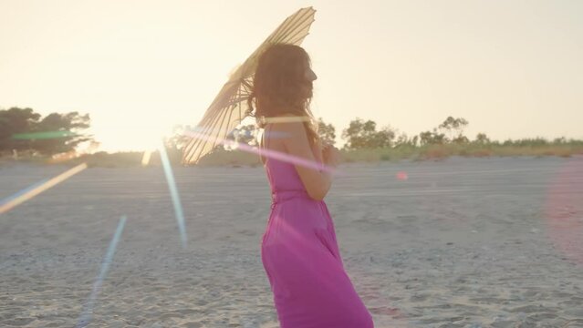  Pink Dressed Girl with umbrella Walk On The Beach with sunset behind her