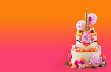 Tall and bright unicorn cake with chocolate, meringue swirls and cupcakes. Isolated on pink background with copy space on a side. Horizontal