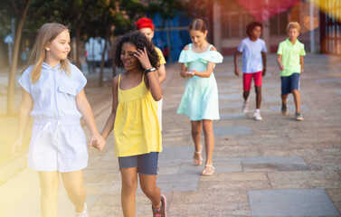 Two cheerful cute preteen girls enjoying walk along city street on summer day..