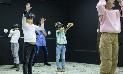 Modern cheerful tweenagers wearing virtual reality goggles playing video games together