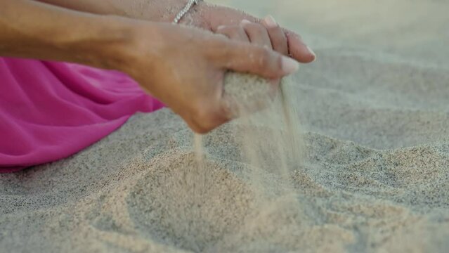Hand Of A Girl in pink dress Touch Sand on the beach near the ocean