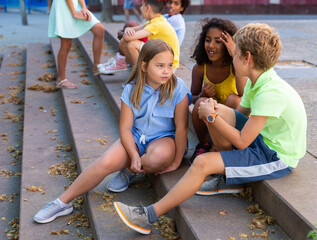 Group of kids sitting on stairs outdoors and talking. Boy and girls having conversation.