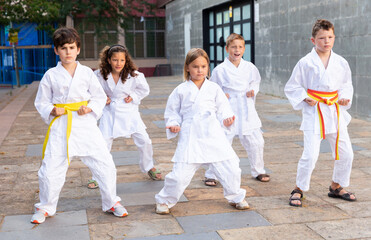 Focused tweenagers exercising new karate moves during group class in courtyard of sports school in summer..