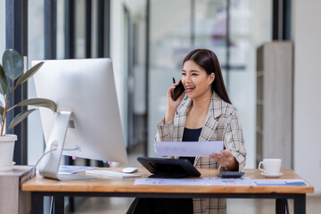 Obraz premium Asian woman entrepreneur busy with her work in the office. Young Asian woman talking over phone or cellphone while sitting at her desk. 