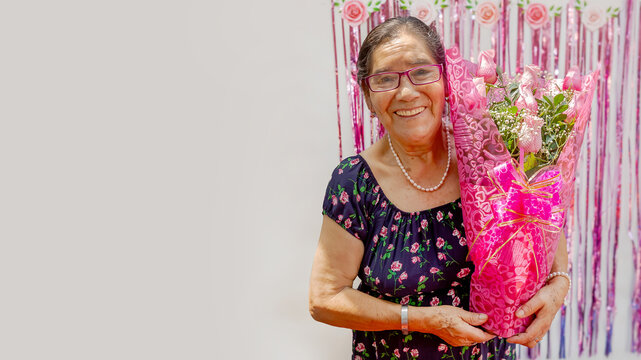 A woman holds a bouquet of flowers and smiles with great happiness. The flowers are pink and arranged in a vase. Concept of celebration, Mother's Day. copyspace......