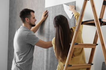 Couple hanging stylish gray wallpaper in room