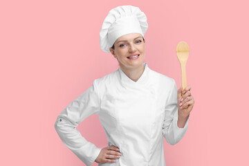 Happy chef in uniform holding wooden spoon on pink background