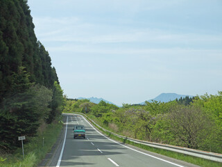 Travelling on Kyushu, driving to distant Mount Aso famous volcano caldera contour on lonely road with lush green grass valley on roadsides on sunny day