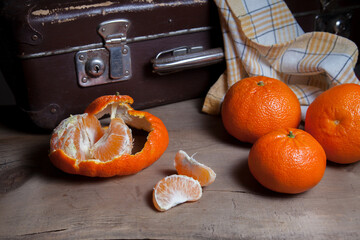 Unpeeled round ripe orange mandarins or tangerines and slices of peeled mandarin on wooden board.