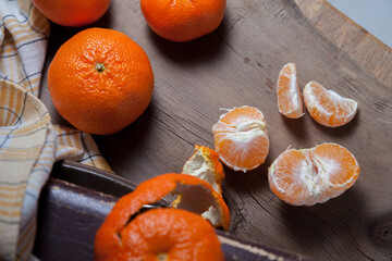 Unpeeled round ripe orange mandarins or tangerines and slices of peeled mandarin on wooden board.