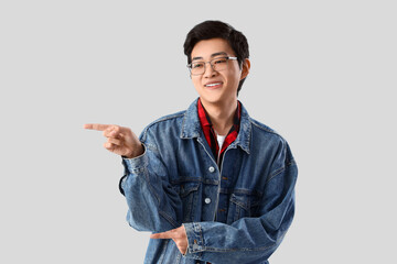 Young Asian man pointing at something on light background