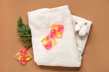 Capsules with laundry detergent, clean towel and conifer branch on brown background