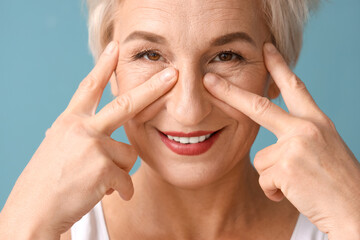 Mature woman doing face building exercise on blue background, closeup