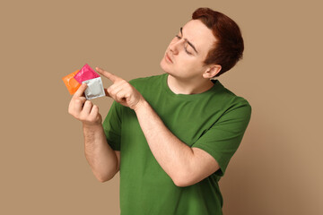 Young man with condoms on beige background. Safe sex concept