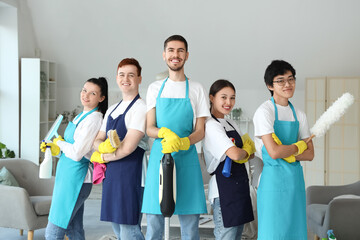 Team of young janitors with cleaning supplies in room