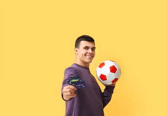 Young man with soccer ball and credit cards on yellow background