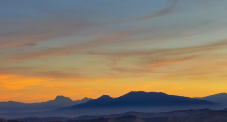 Luminoso tramonto arancio e ocra sopra le montagne italiane