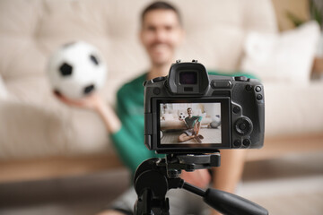 Sporty happy male blogger with soccer ball recording video at home