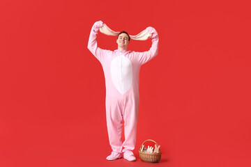 Happy young man in Easter bunny costume holding ears on red background
