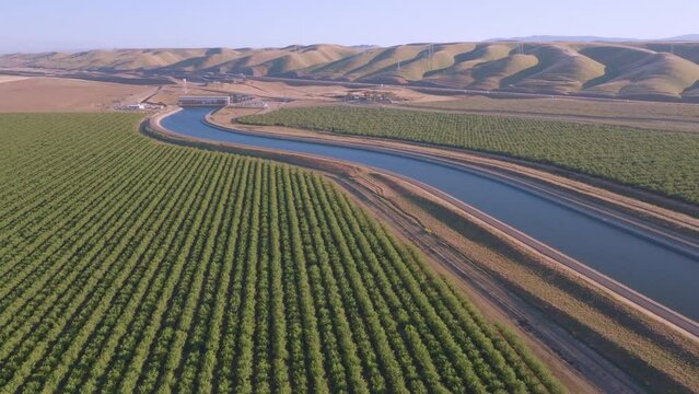 Aerial view of a wide irrigation canal curving through orchards at sunset