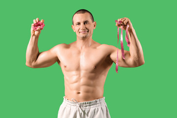 Male bodybuilder with tape measure clutching doughnut on green background