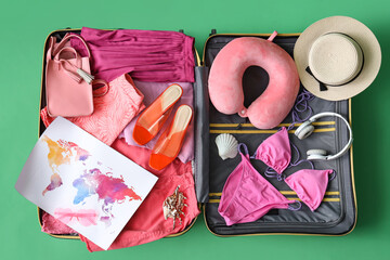 Open suitcase with female clothes, beach accessories, headphones and world map on green background