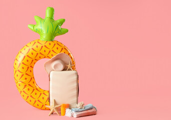Suitcase, beach accessories, inflatable ring and decor on pink background