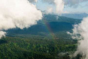 Aerial View of Lush Green Forests and Hills with Clouds and a Faint Rainbow.