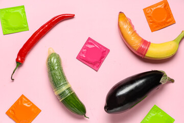 Condoms with fruits and vegetables on pink background. Sex education