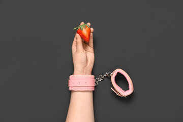 Female hand in handcuffs with fresh strawberry on black background. Sex education