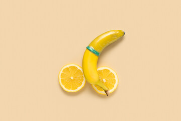 Cut lemons and fresh banana in condom on beige background. Sex education