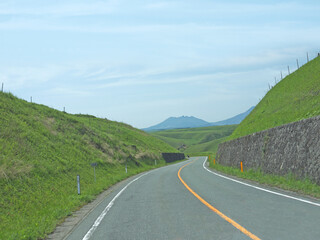 Travelling on Kyushu, driving to distant Mount Aso famous volcano caldera contour on lonely road with lush green grass valley on roadsides on sunny day
