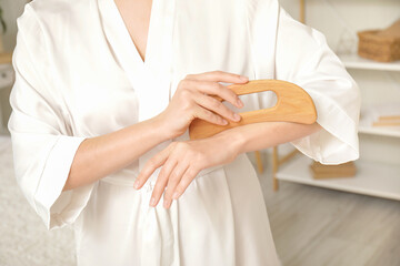 Young woman massaging her arm with wooden scraper in bedroom, closeup