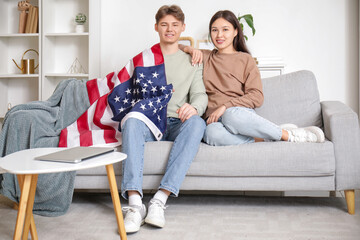 Young couple with flag of USA sitting on sofa at home