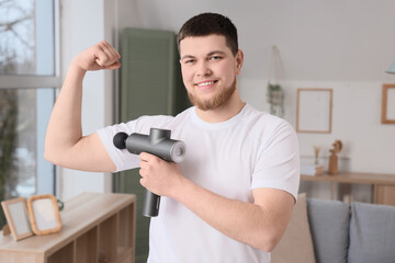 Sporty young man massaging his arm with percussive massager at home