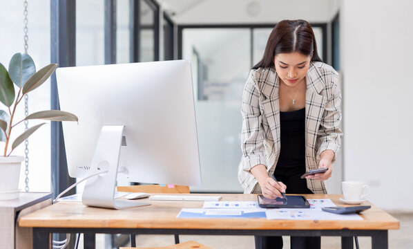 Young happy professional business asian woman employee sitting at desk working on laptop in modern corporate office interior. Smiling female worker using computer technology typing browsing web.