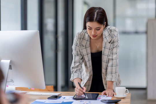 Young happy professional business asian woman employee sitting at desk working on laptop in modern corporate office interior. Smiling female worker using computer technology typing browsing web.