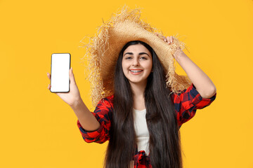 Beautiful young happy woman with mobile phone on yellow background. Festa Junina (June Festival)...