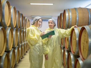 Engineer technicians staff woman two person smiling talk and inspect check quality control working job in wine vats barrels on modern technology winemaking factory  industry plant in warehouse.