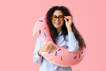 Happy female office worker with inflatable ring on pink background. Summer vacation concept