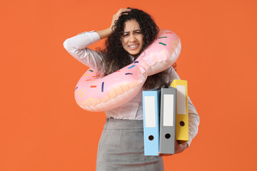 Stressed female office worker with inflatable ring and folders on orange background. Summer...